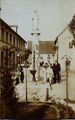 Die Familie Schertl posiert neben der Mariensäule und dem davor befindlichen Brunnen. Links zu sehen das einstige Knabenschulhaus, rechts die damalige Sakristei der Pfarrkirche. Das Foto entstand in den 1920er Jahre. Die Figur der Gottesmutter schaut auf diesem Bild Richtung Westen. Später wurde die Säule gedreht und nach Norden versetzt. Heute schaut die Figur nach Norden.[3]